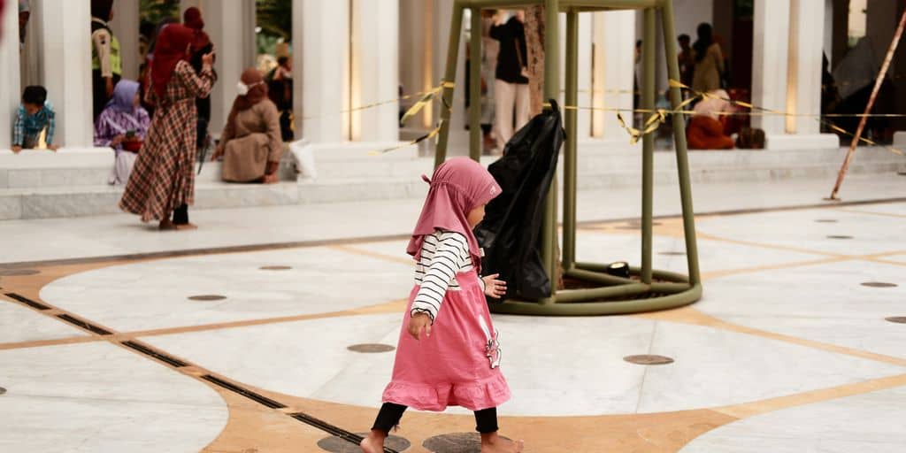 a little girl in a pink hijab walking through a building