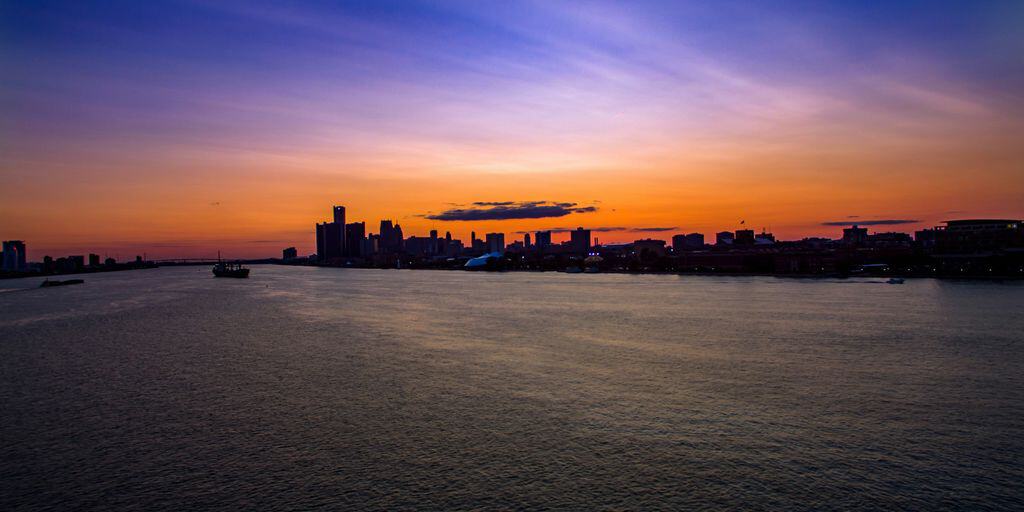 silhouette of city buildings and boat above water at golden hour